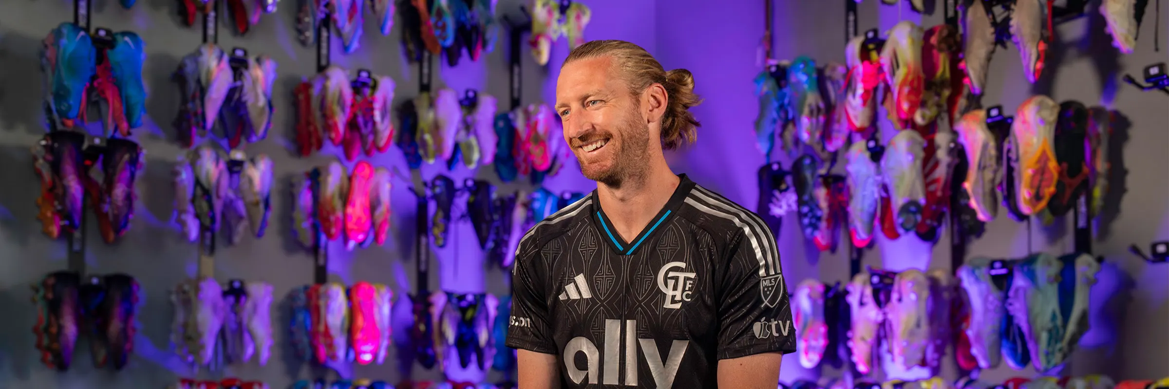 Charlotte FC defender Tim Ream sits on a bench in front of two walls of soccer cleats.