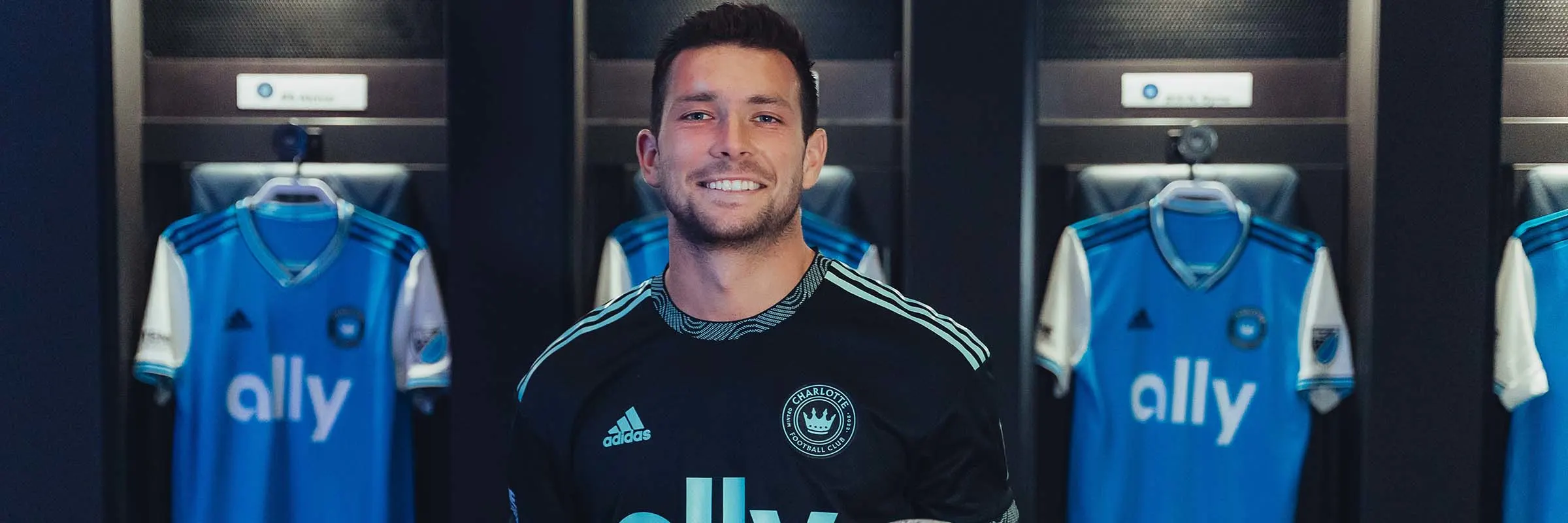 Brandt Bronico poses in front of Charlotte FC jerseys in a locker room