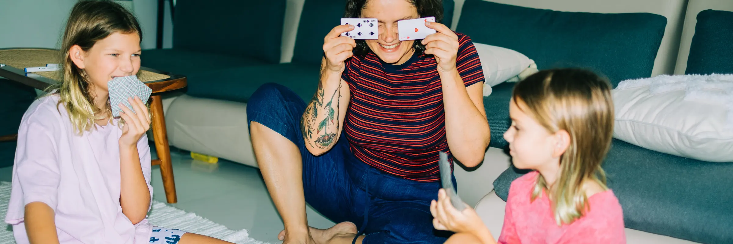 Mom and two daughters sitting on the floor playing card games.  