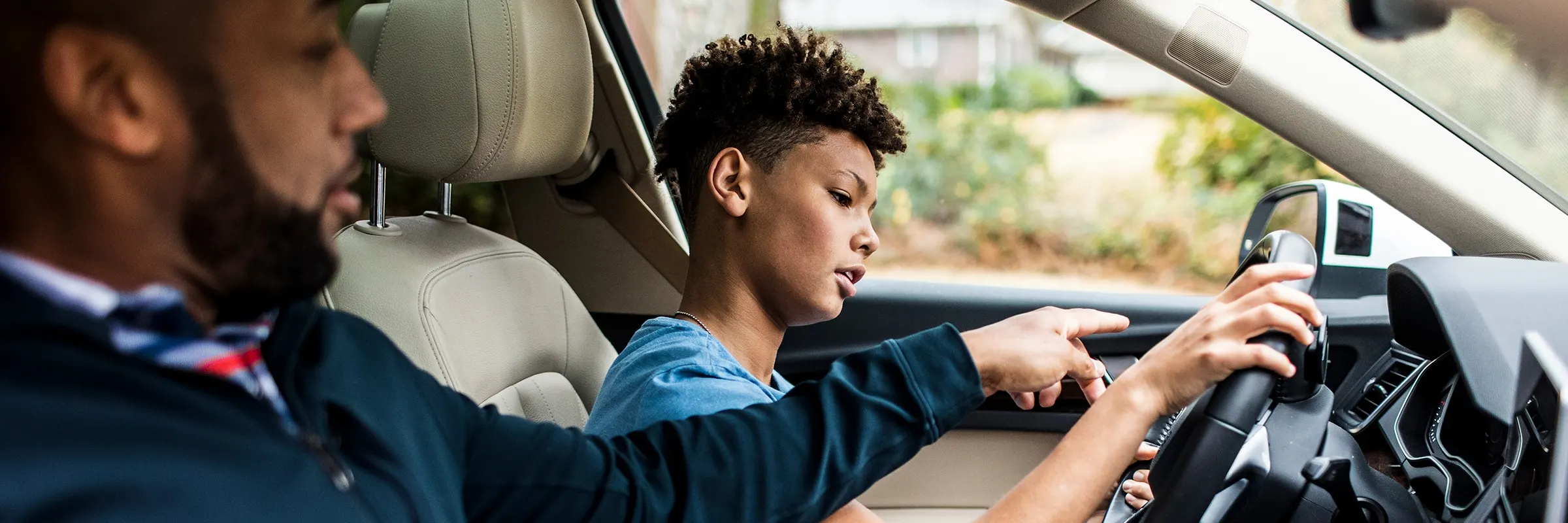 Father sits in the passenger seat of a vehicle and teaches his son how to drive.