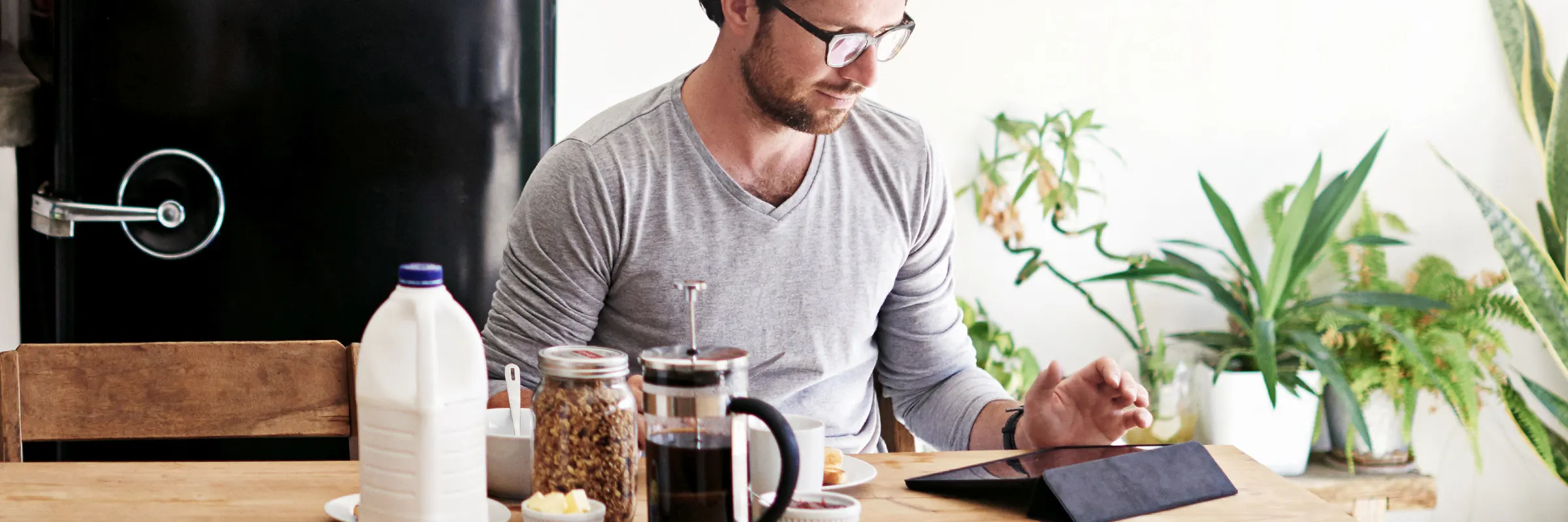 A man sits at his kitchen table enjoying coffee and breakfast while looking at his tablet.