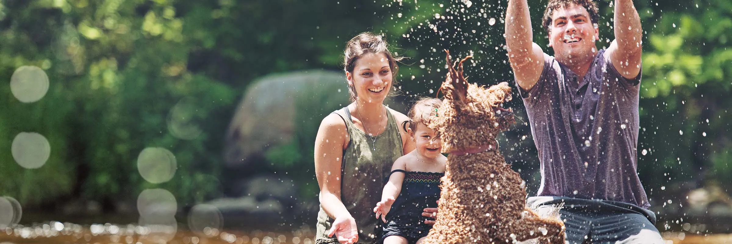 Family of three plays with water hose outside with their dog. 