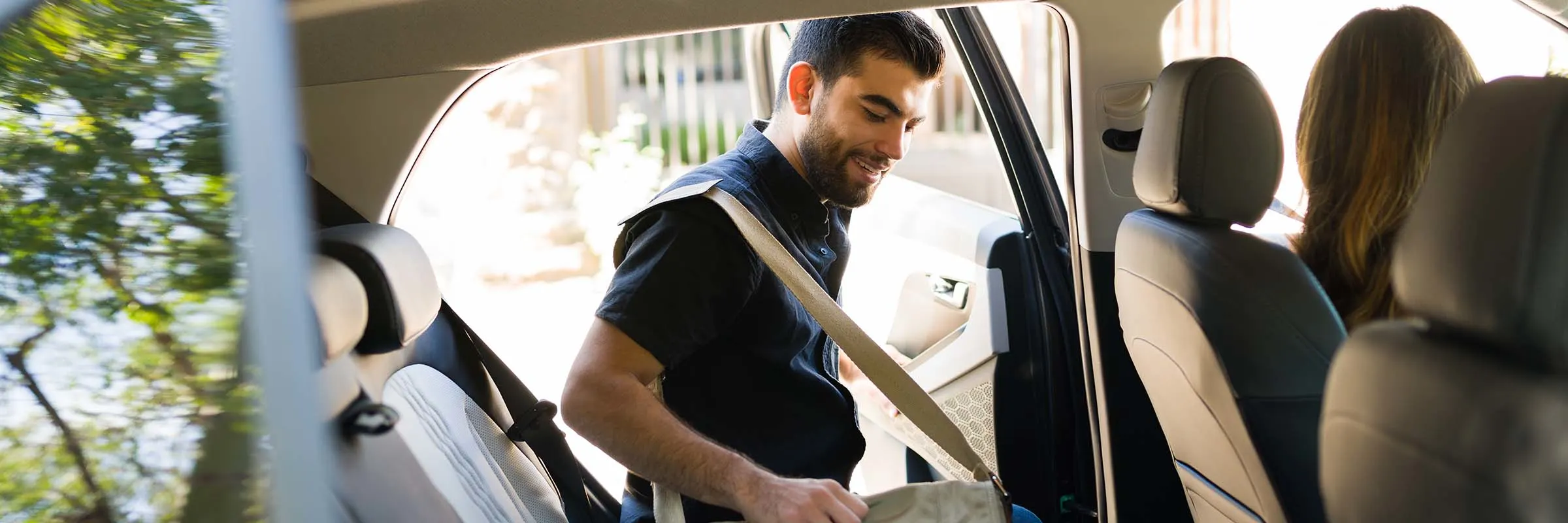 Man with a messenger bag gets into the back seat of a car