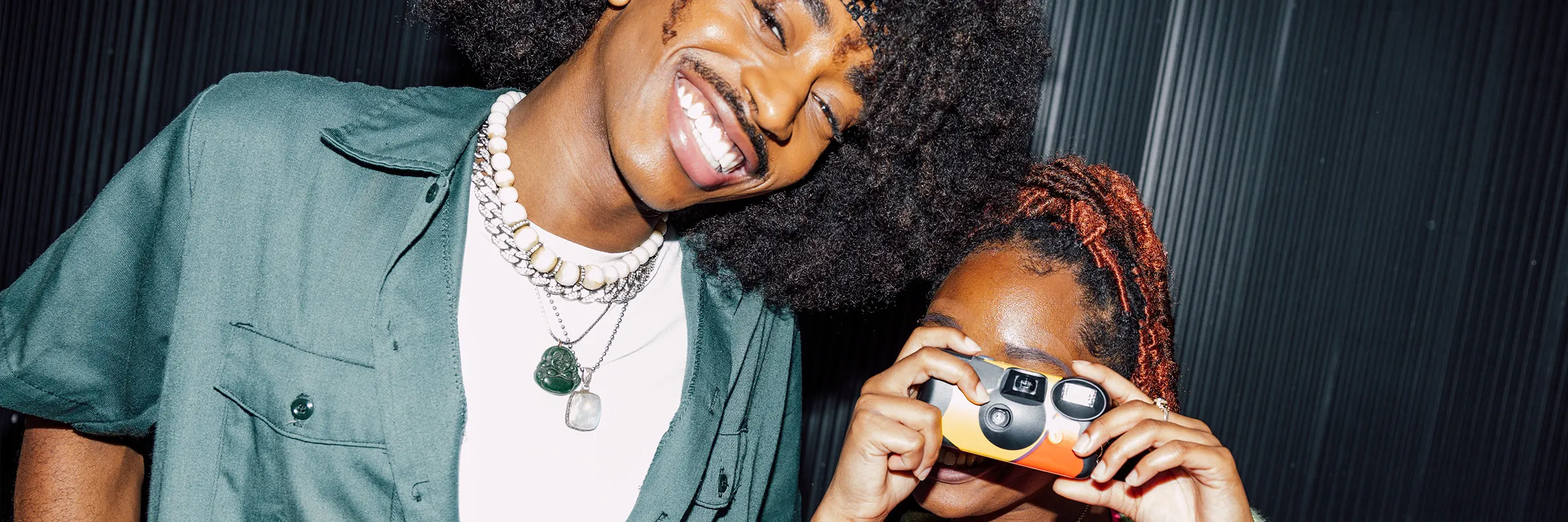 Young man and woman smiling for the camera. The woman is using a disposable camera. 
