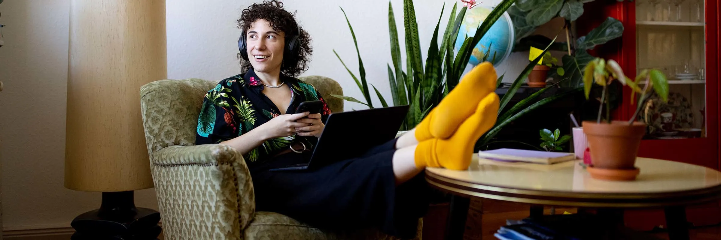  A person listens to music while sitting in a chair with a phone and laptop.