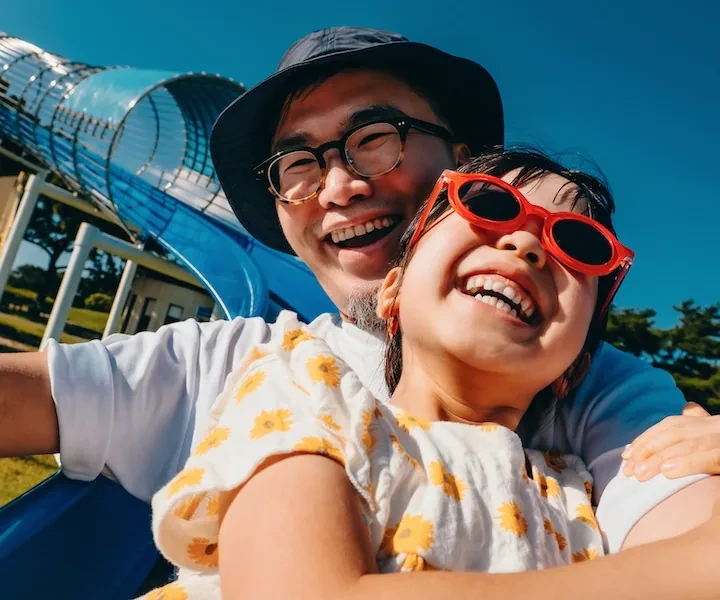 A young father and daughter smiling as they go down a slide together