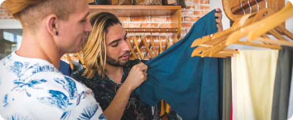 Man with long, bleached hair peruses clothing on hangers.