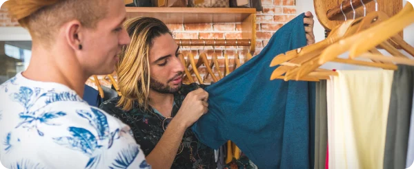 Man with long, bleached hair peruses clothing on hangers.