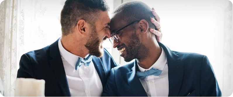 Two men at a formal event put their foreheads together, smiling.