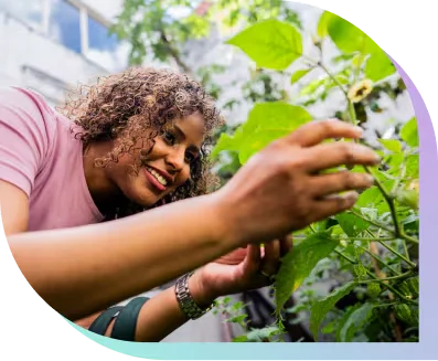a smiling woman checks on a plant in her garden