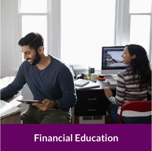 a woman sitting down working at a computer, and a man sitting next to her holding a tablet.