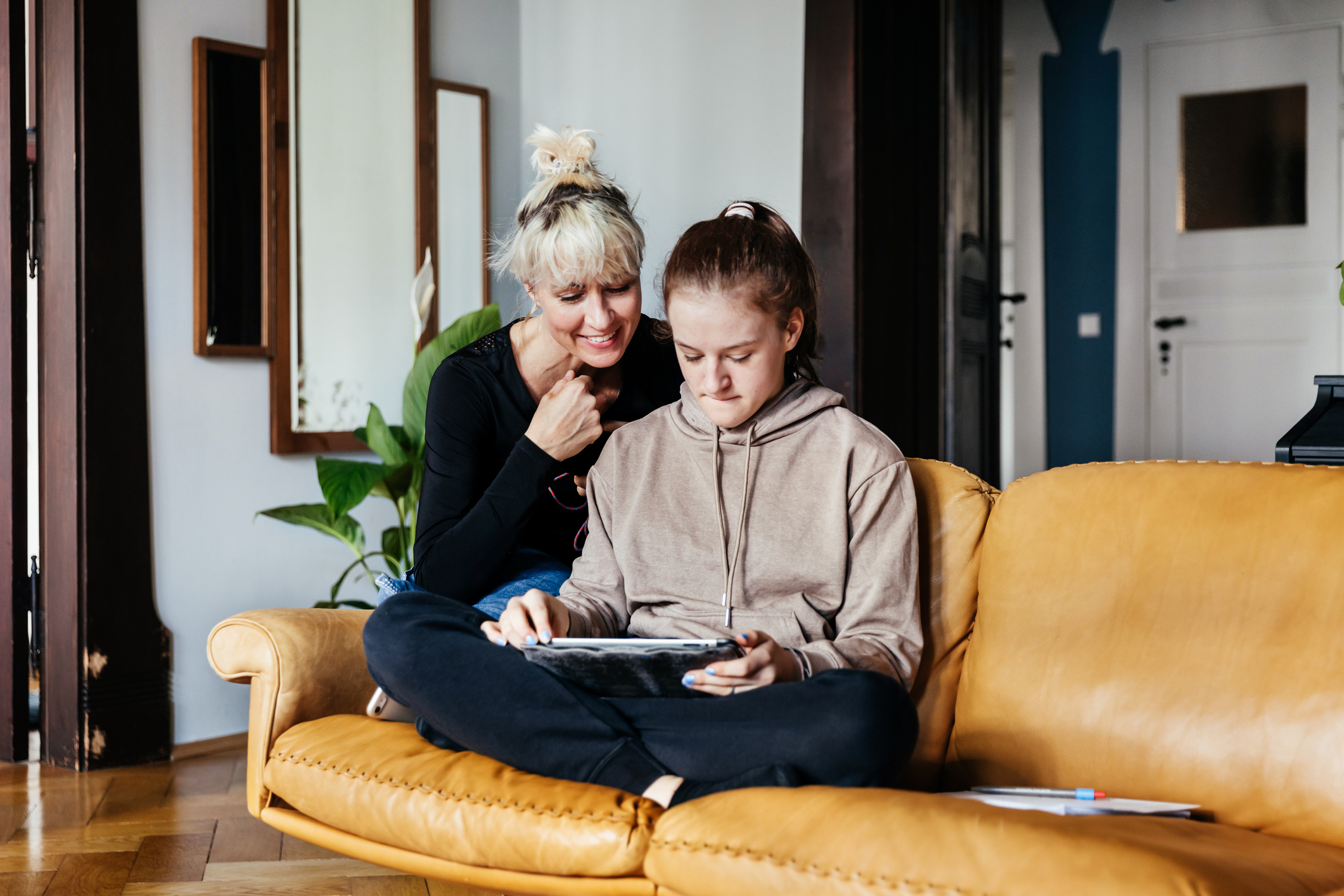 Mother and daughter sitting on a couch and looking at a tablet.