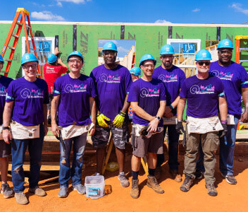 a group of male and female Ally employees wearing hardhats and volunteering at a building site