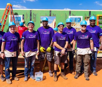 a group of male and female Ally employees wearing hardhats and volunteering at a building site