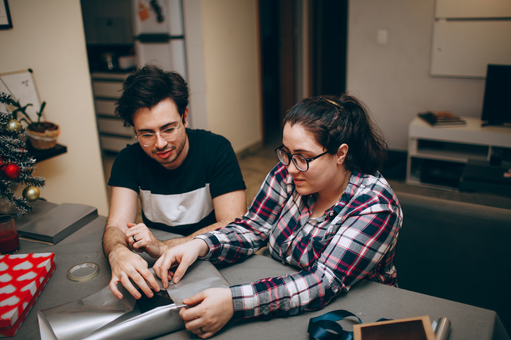 Couple sits at a table while wrapping gifts together.