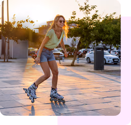 A woman in summer clothing and sunglasses rollerblades outside at sunset.