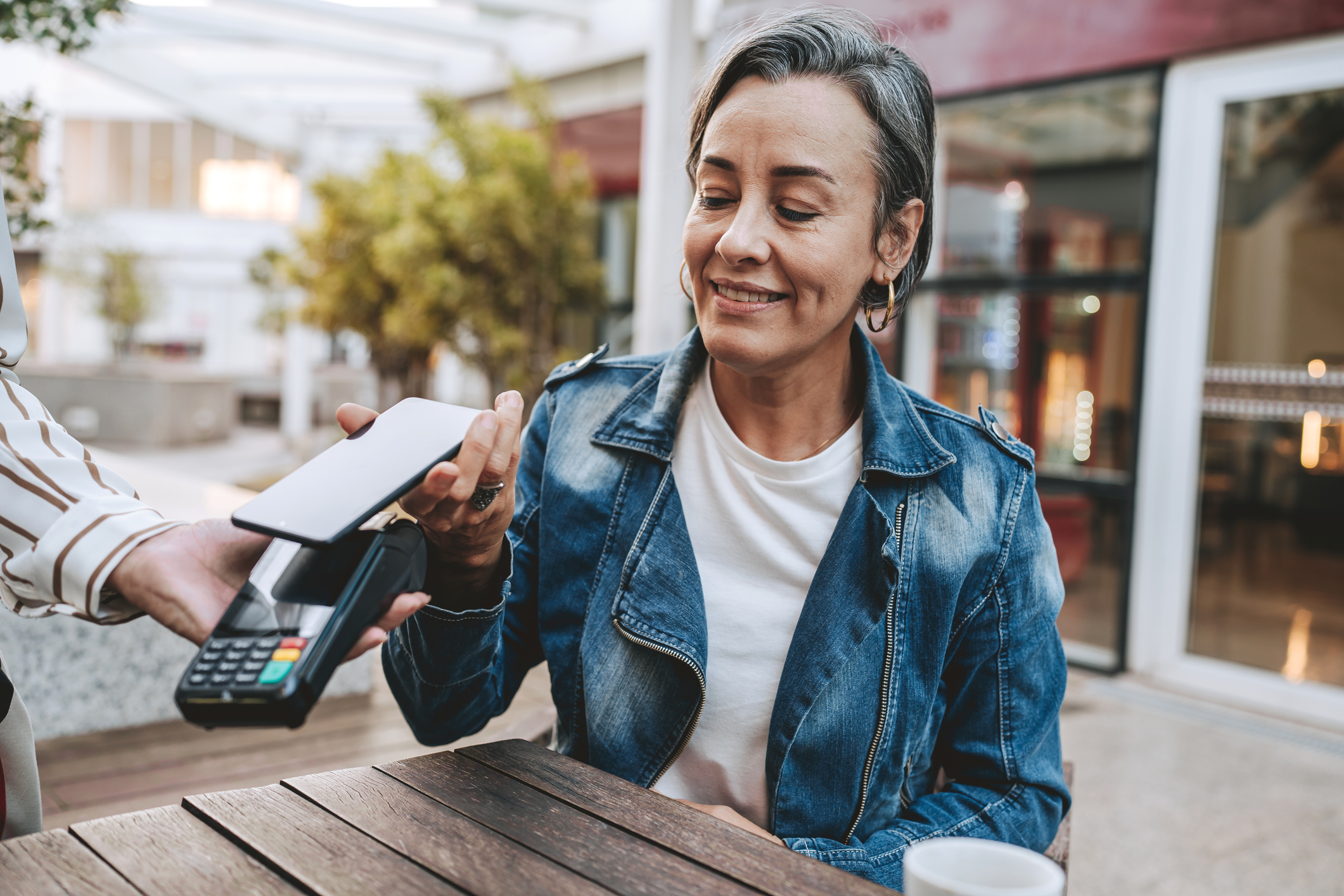A woman using mobile tap-to-pay at an outdoor restaurant.
