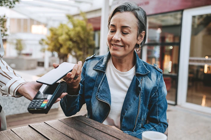 A woman using mobile tap-to-pay at an outdoor restaurant.