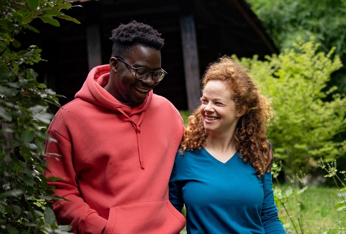 Happy couple walks through the wooded yard behind their house.