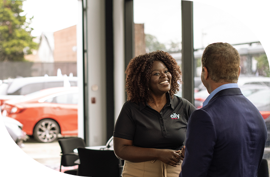 a smiling woman Ally employee shaking the hand of a dealer at a dealership