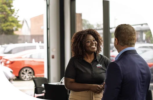 a smiling woman Ally employee shaking the hand of a dealer at a dealership