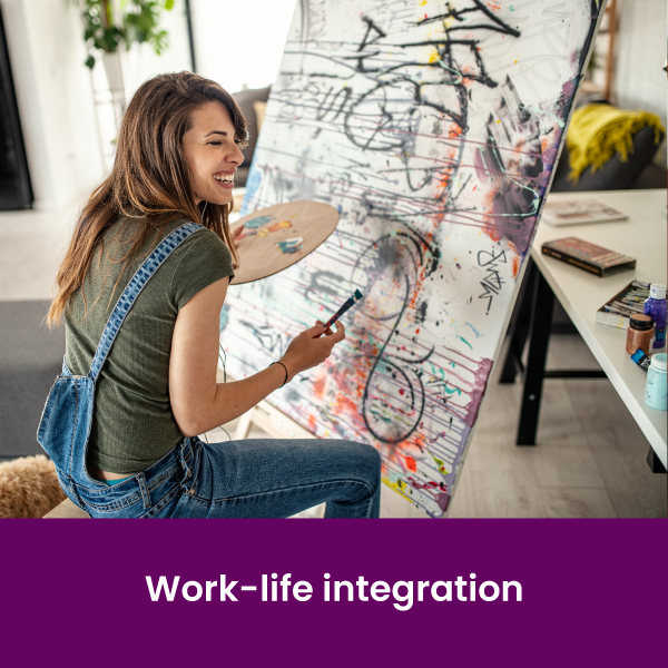 a smiling woman holding an easel sitting in front of a large canvas and painting