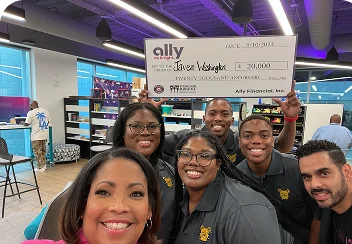 a group of young male and female college students posing with a check presented to them by Ally employees.