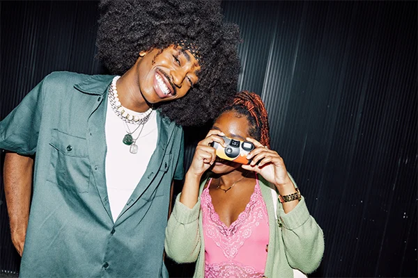 Young man and woman smiling for the camera. The woman is using a disposable camera.