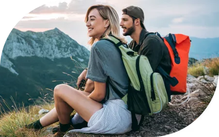 A backpacking couple sit on a mountaintop, smiling and taking in the view.