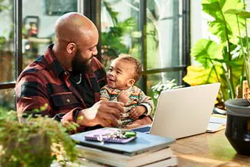 Father and young child sitting at kitchen table looking at the computer