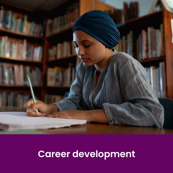 a woman sitting at a desk in a library holding a pencil and writing in a notebook