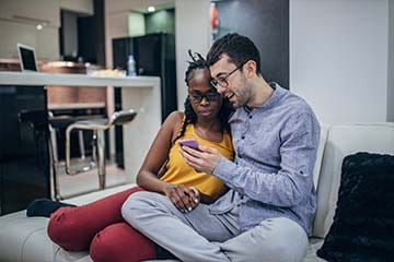 A man and a woman sit closely on a couch while looking at a smartphone
