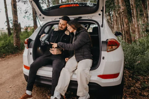 Couple parked on the side of a trail, sitting in the back of their white suv looking at video camera