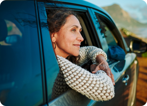 A woman with a peaceful gaze peers out the window from the back seat of a vehicle.