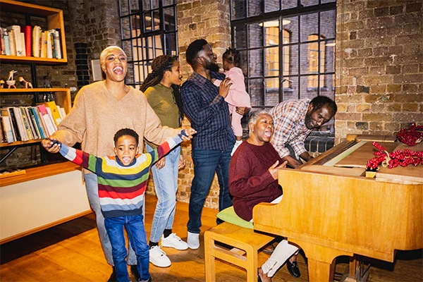 Multi-generational family gathered around a piano and singing.