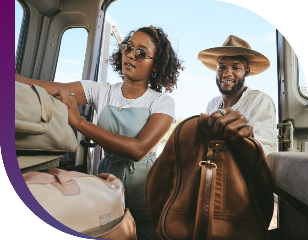 A couple excitedly packs their car with suitcases for a trip.