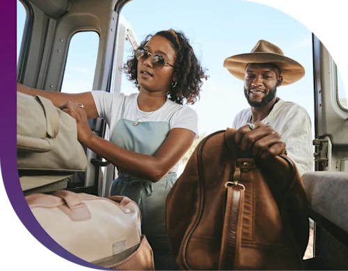 A couple excitedly packs their car with suitcases for a trip.