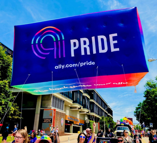 A spirited group of parade participants display a large and colorful Ally Pride balloon.