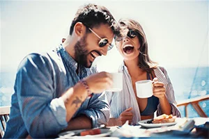 Young couple laughing and drinking coffee waterside.