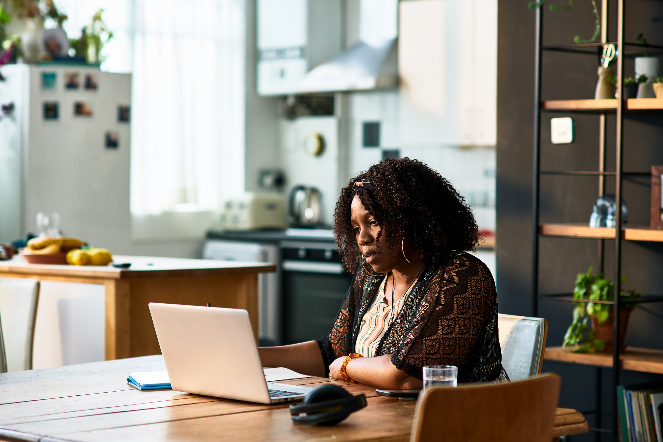A woman sits at a counter in the kitchen facing a large window while looking at her phone.