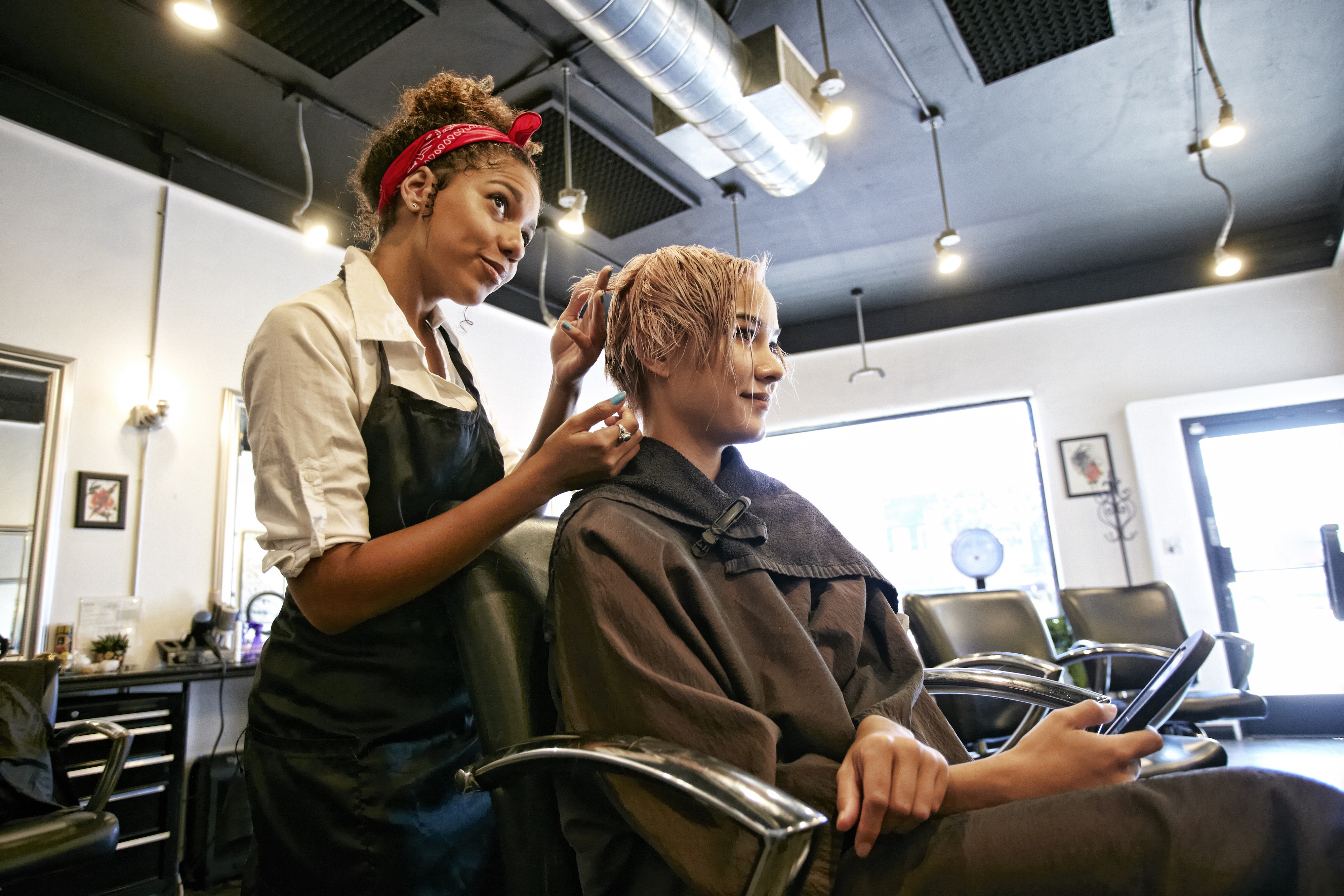 A hair stylist stands behind a customer while they cut their hair