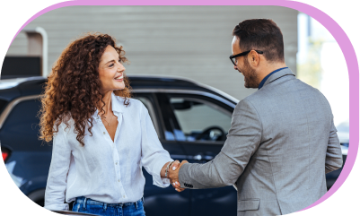 A dealership employee and customer shaking hands beside a parked car.