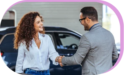 A dealership employee and customer shaking hands beside a parked car.