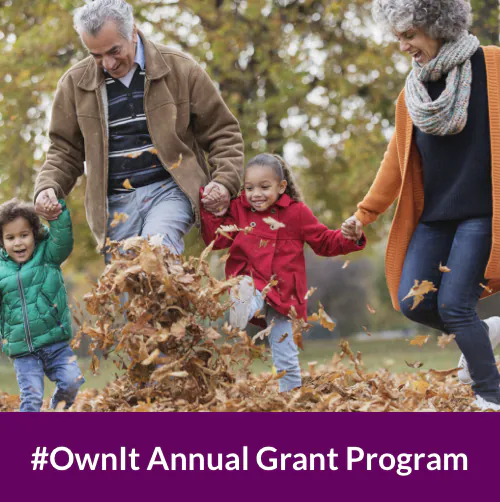 an older man and woman holding hands with their grandson and granddaughter as they leap through a pile of brown leaves on an autumn day