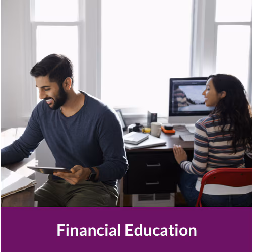 a woman sitting down working at a computer, and a man sitting next to her holding a tablet.