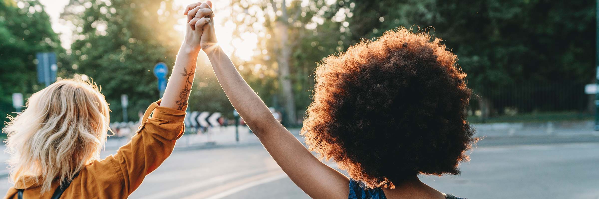 Image of two people holding their joined hands in the air, looking towards the sun. 