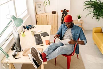 Image of a man reading a book with his feet up on his desk