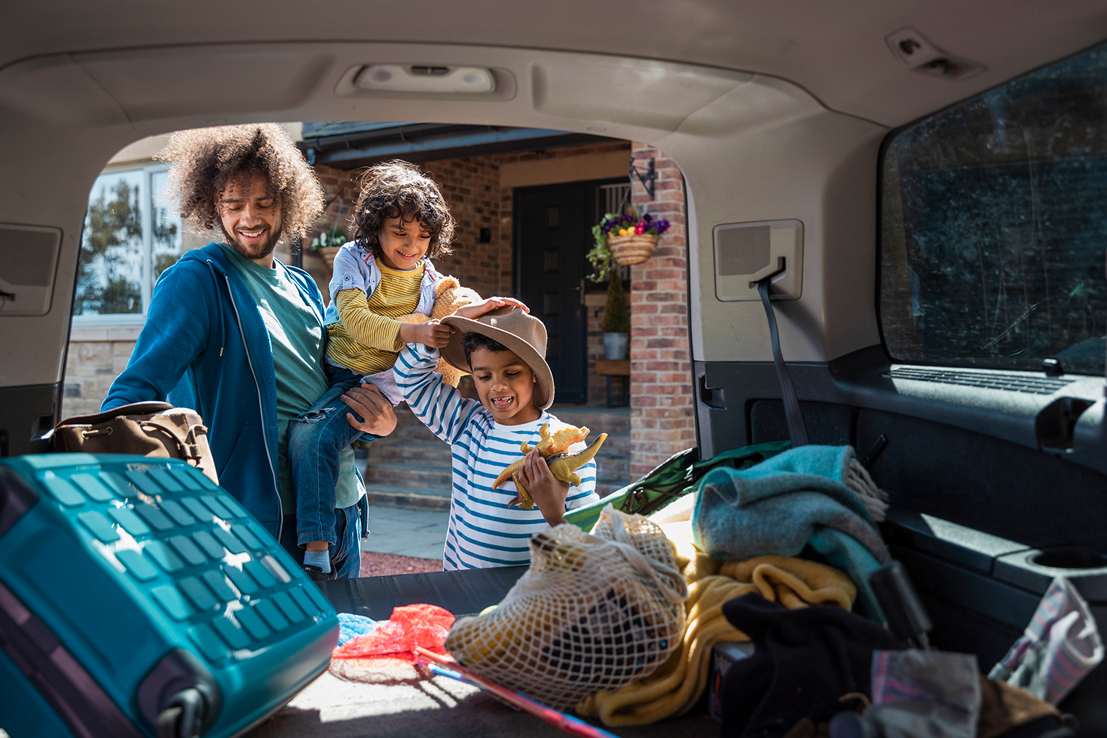 A father and his two young sons pack up the back of their car as they prepare for vacation.