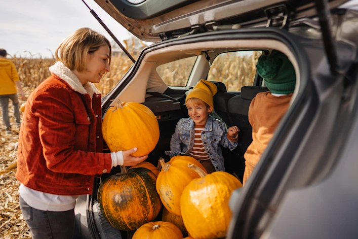 A mother and her two children loading pumpkins into the trunk of her vehicle.