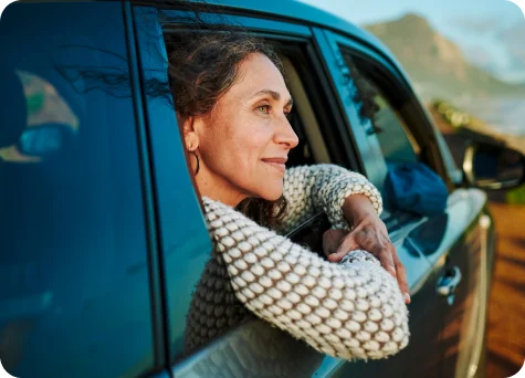 A woman with a peaceful gaze peers out the window from the back seat of a vehicle.